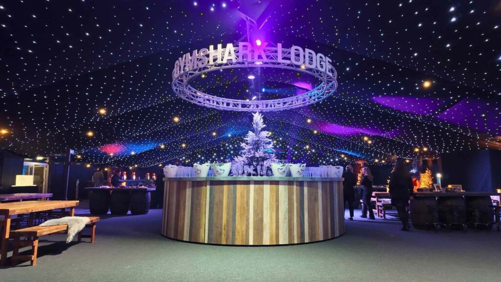 Circular timber bar beneath a lit GYMSHARK LODGE truss ring and starcloth ceiling at a corporate Christmas party