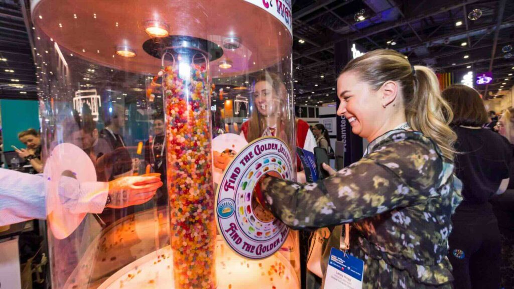 Visitors collecting sweets from a jelly bean waterfall at a busy exhibition stand with find the golden jelly bean signage