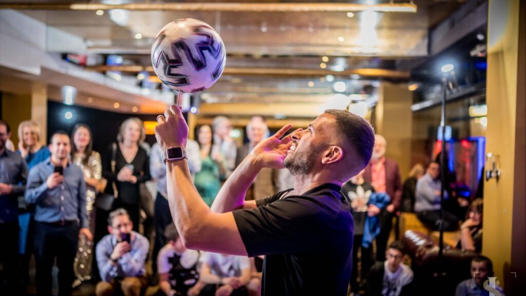 Football freestyler spinning a ball on his finger in front of a seated and standing crowd at a corporate event
