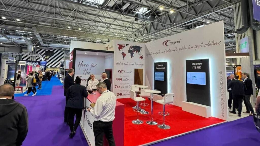 Visitors and exhibitors at a branded Trapeze stand on a busy trade show floor during a live convention