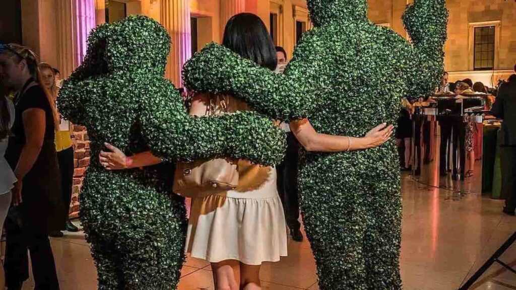 Two walkabout hedge performers posing for a photograph with guests at an indoor event