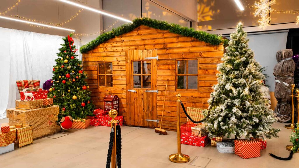 Wooden Christmas grotto cabin with decorated trees and festive lighting installed in a corporate venue