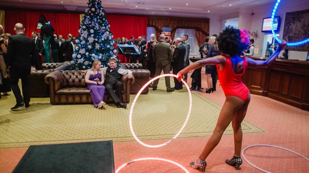 Guests at a corporate Christmas party with a decorated tree, stilt walker and LED hoop performer