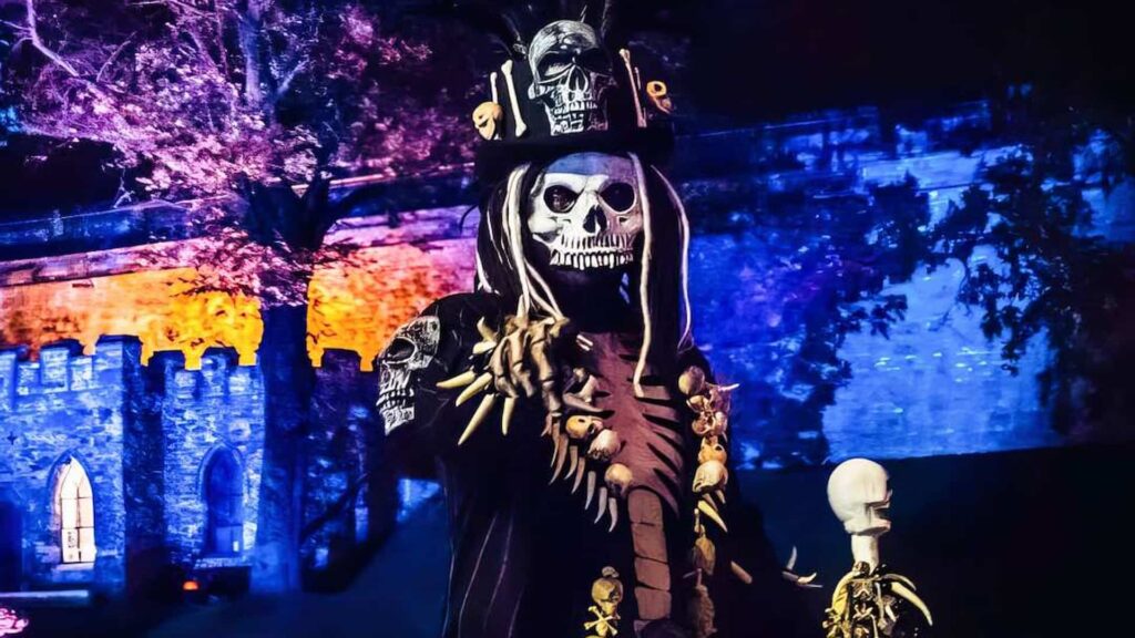 Skeleton walkabout performer in front of a Halloween lighting and projection installation at an evening event