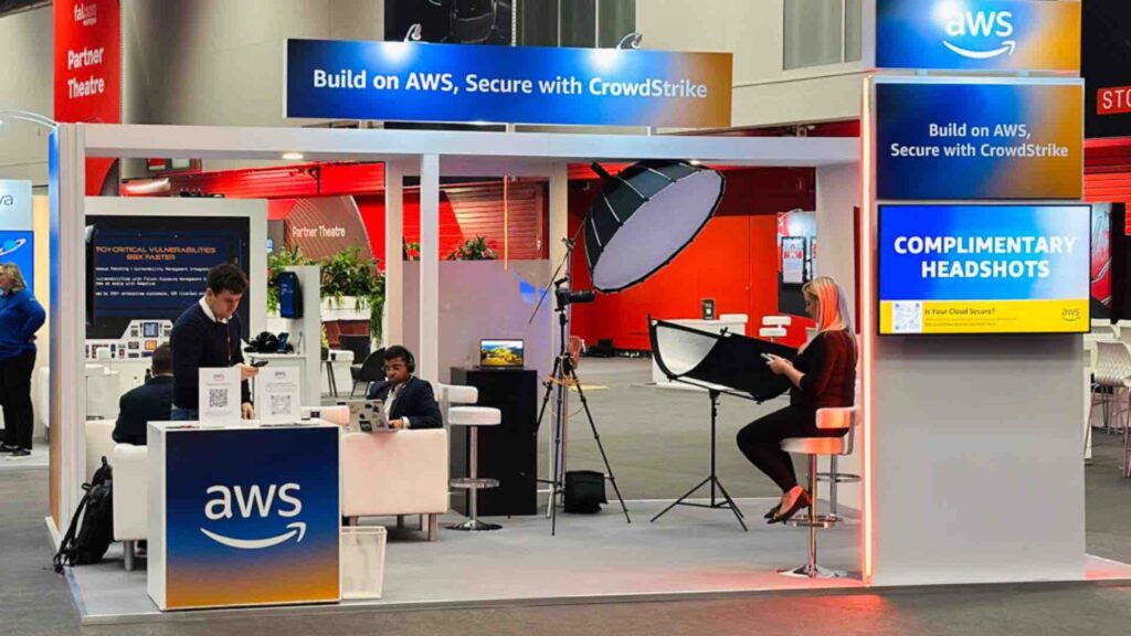 An exhibition stand with branded signage, a professional photography set-up with a large studio light, and a counter with QR code cards.