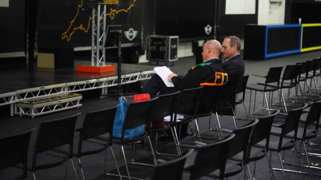 Two members of the event team reviewing printed schedules in an empty seating area during set-up for the MINI brand exhibition