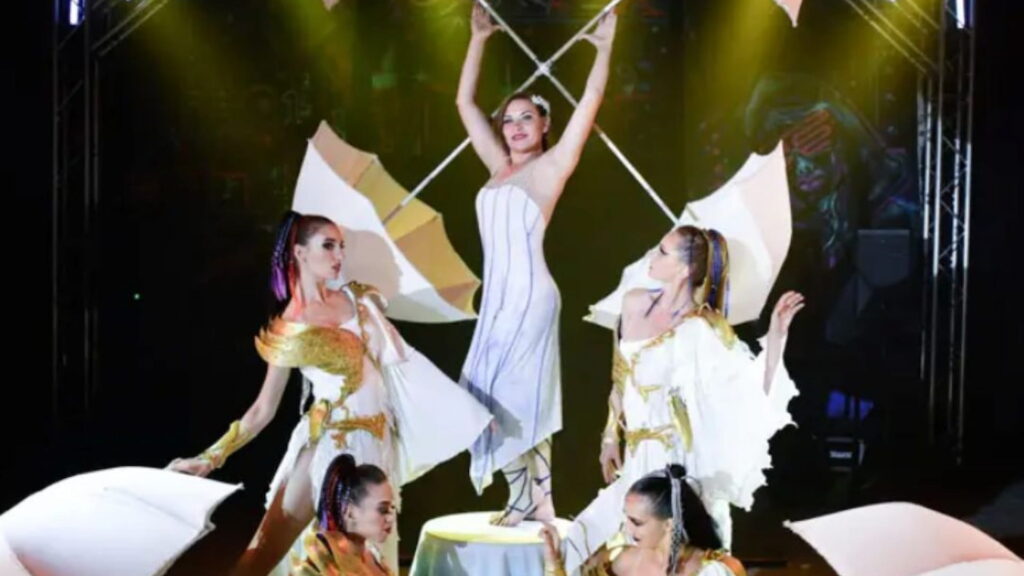 A troupe of circus performers holding umbrellas on stage.