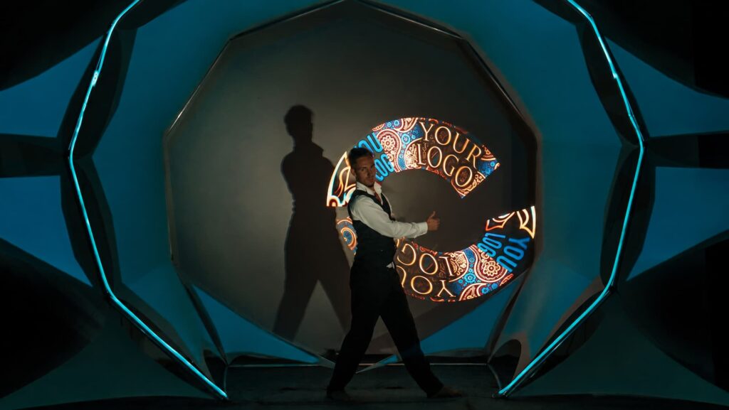 Performer in a waistcoat posing in front of a circular projection showing “Your Logo” artwork.